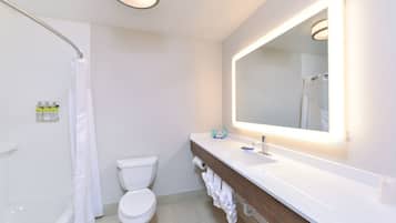 A modern bathroom with a white toilet, a bathtub, a shower, and a vanity with a mirror.
