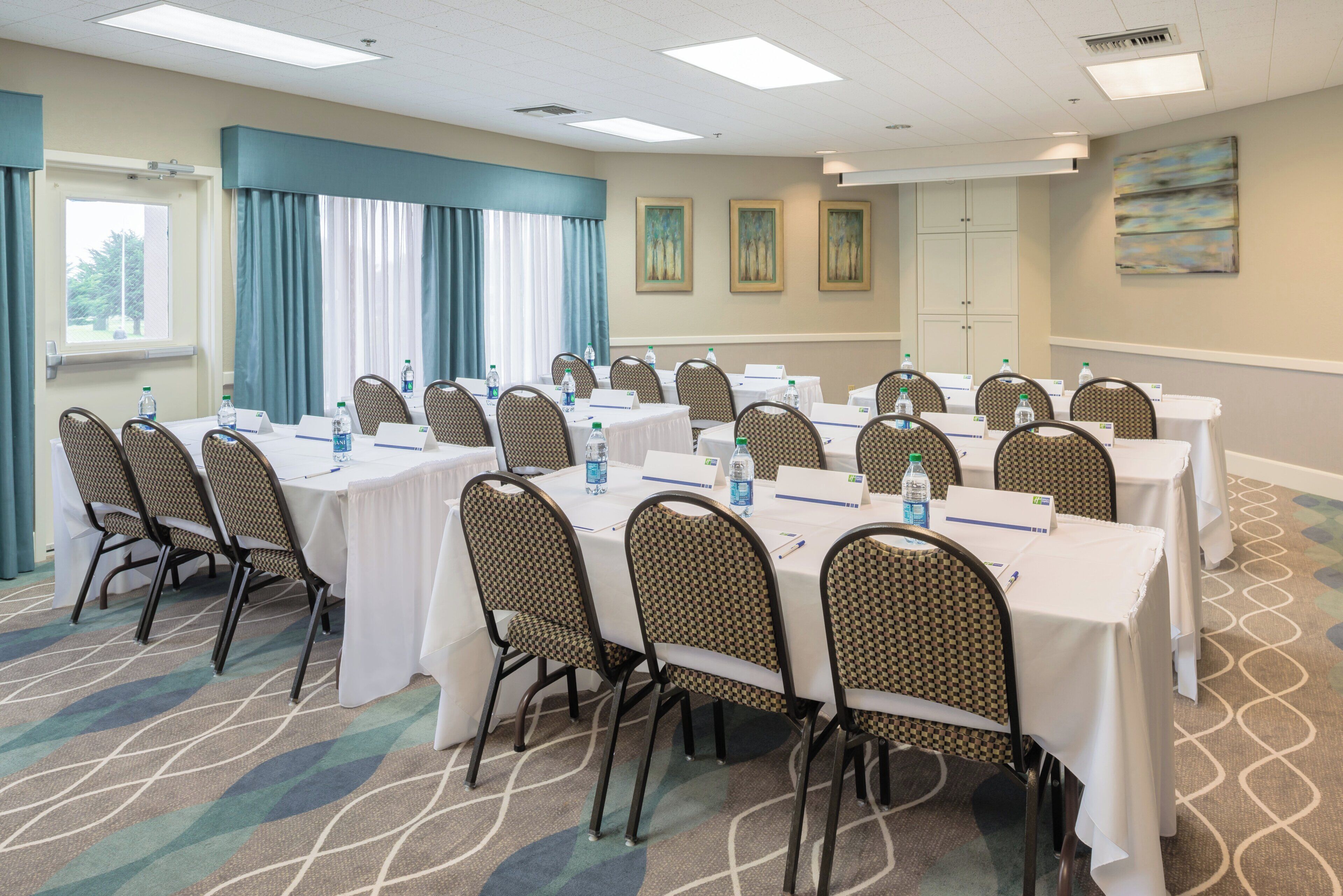 Une salle de conférence équipée de tables et de chaises, de bouteilles d’eau et de plaques nominatives.