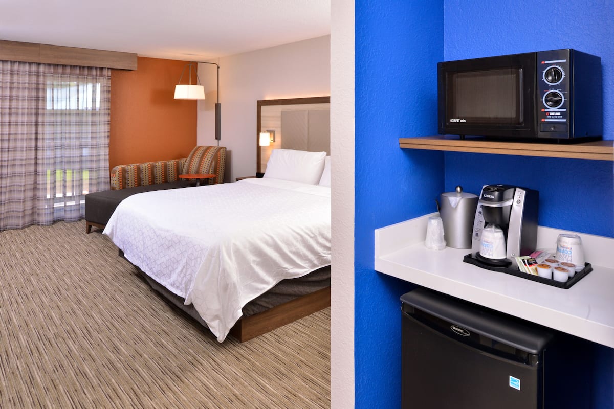 A hotel room with a bed, a desk with a microwave, a coffee maker, and a mini fridge.