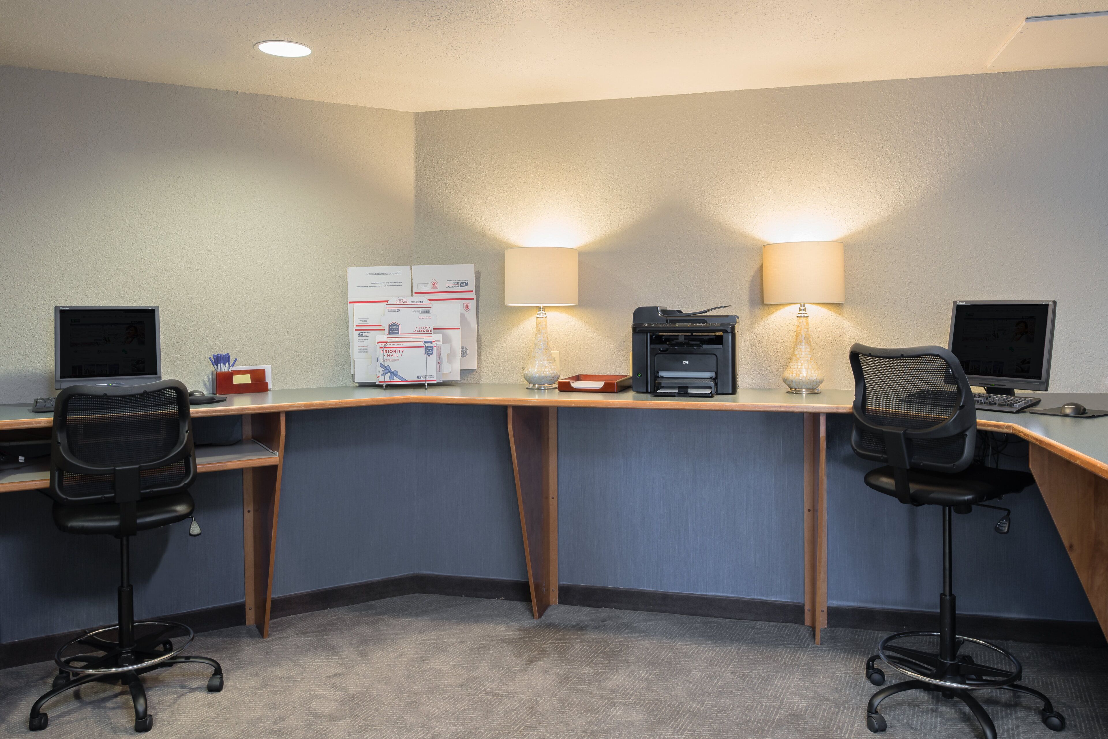 A hotel office with three desks, each with a computer and a lamp.