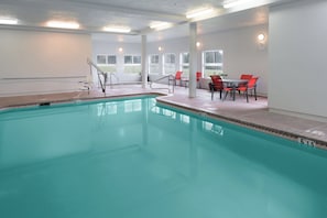 A swimming pool with a lifeguard chair, a table with chairs, and a clock on the wall.