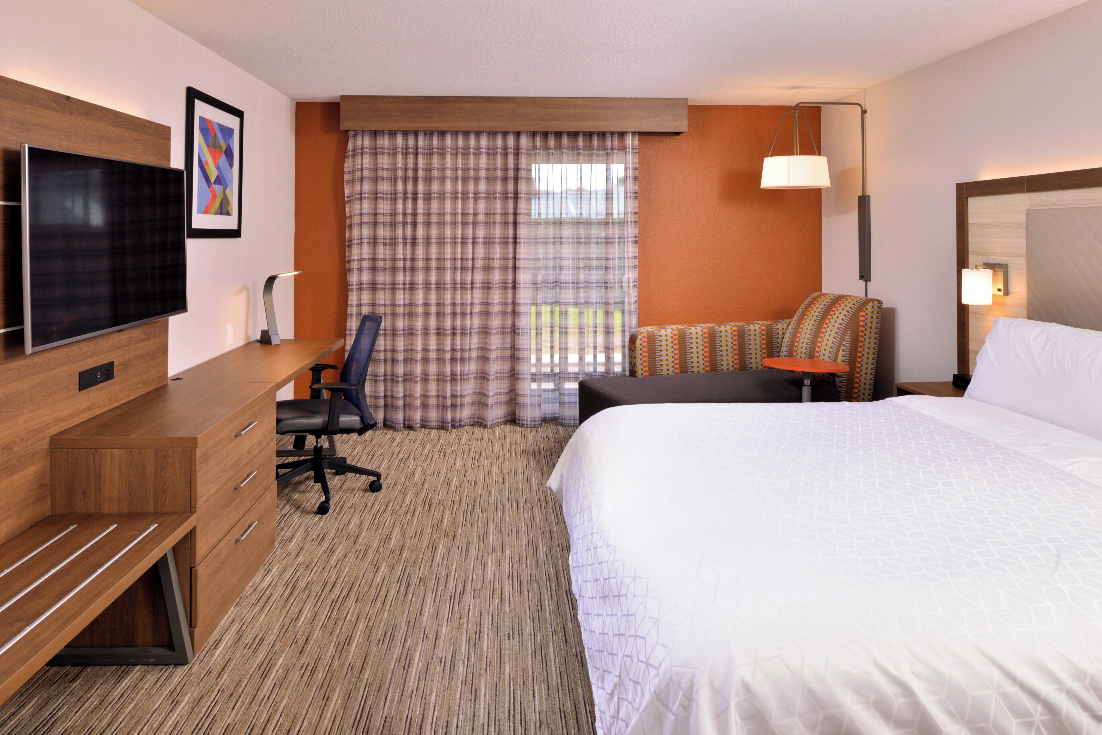 A hotel room with a bed, a desk, a chair, a television, and a window with curtains.