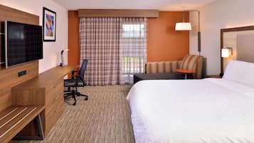 A hotel room with a bed, a desk, a chair, a television, and a window with curtains.