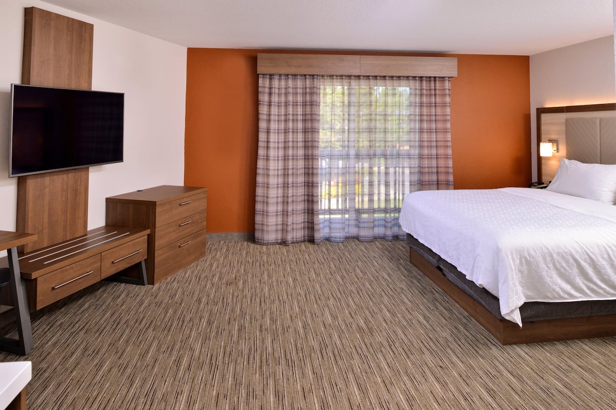 A hotel room with a bed, a TV mounted on the wall, a wooden dresser, and a window with plaid curtains.