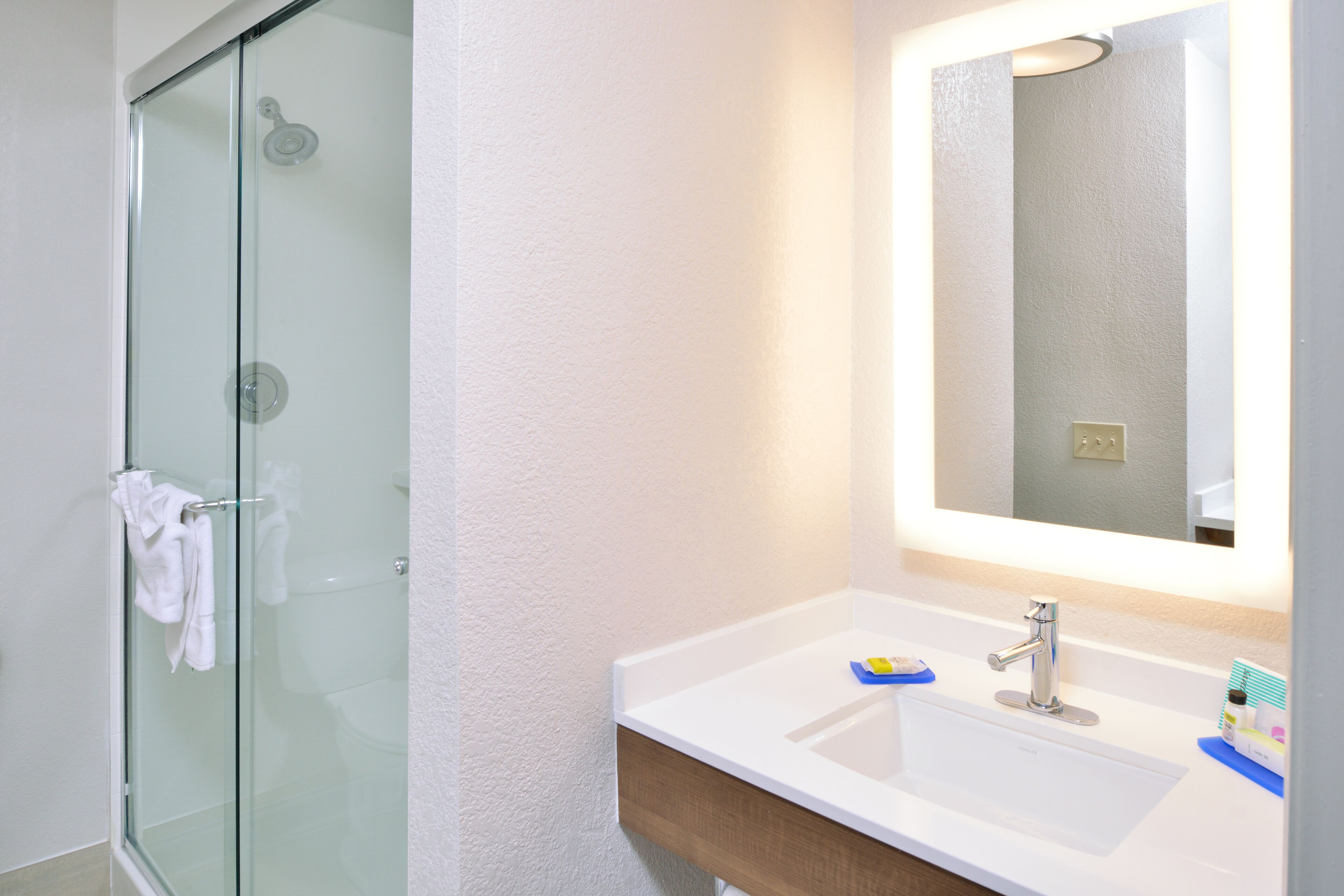 Un baño moderno con cabina de ducha de vidrio, un lavamanos blanco con espejo y artículos de aseo sobre el borde.