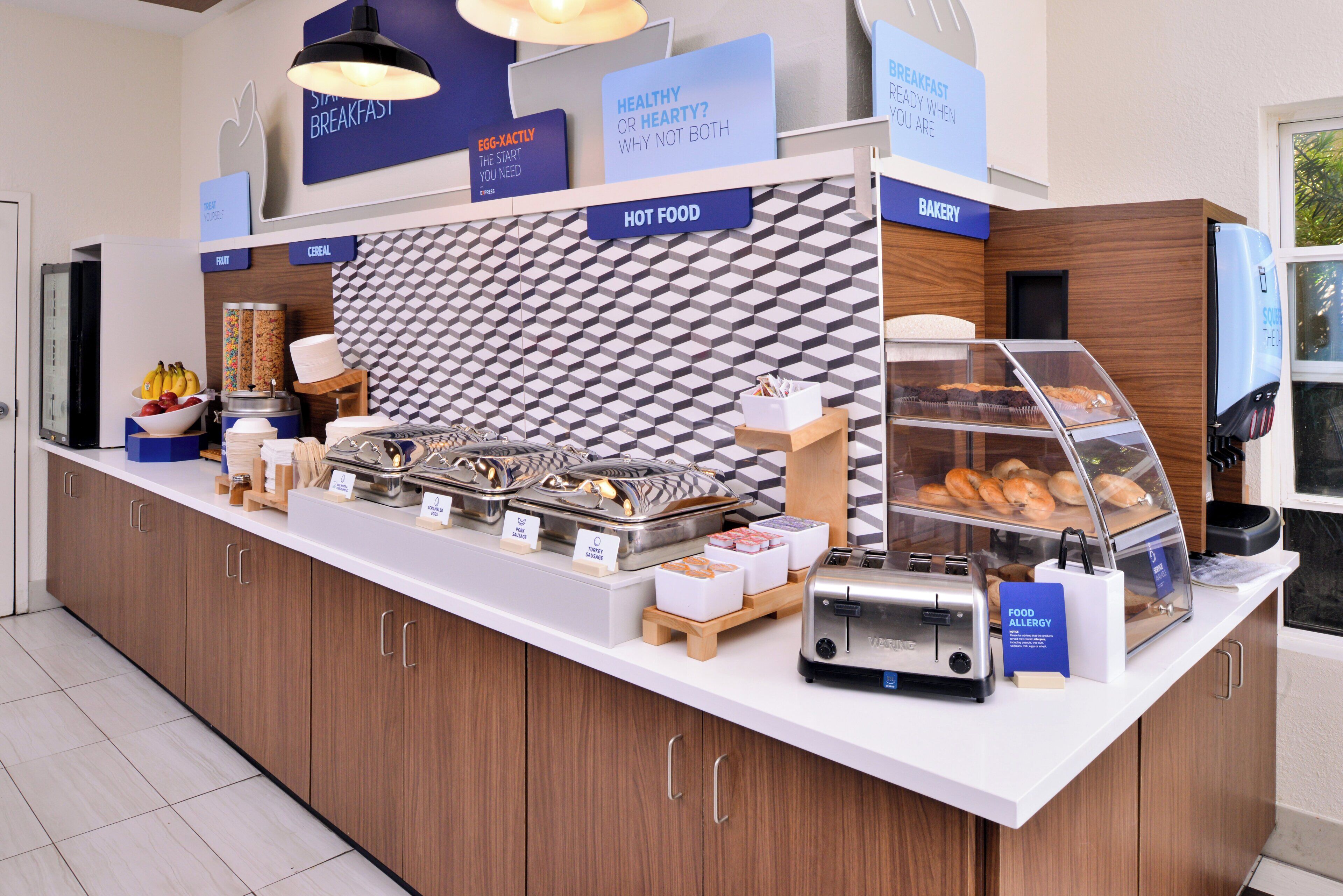 A breakfast station with labeled food options, a bakery display, and a toaster.