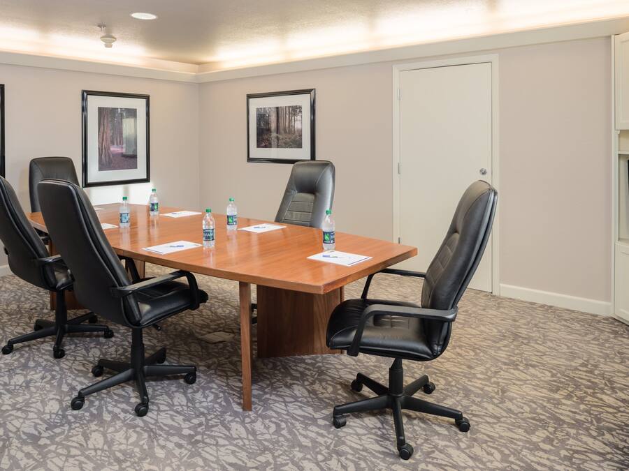 A conference room with a wooden table, black chairs, water bottles, framed pictures on the wall, and a television on the right.