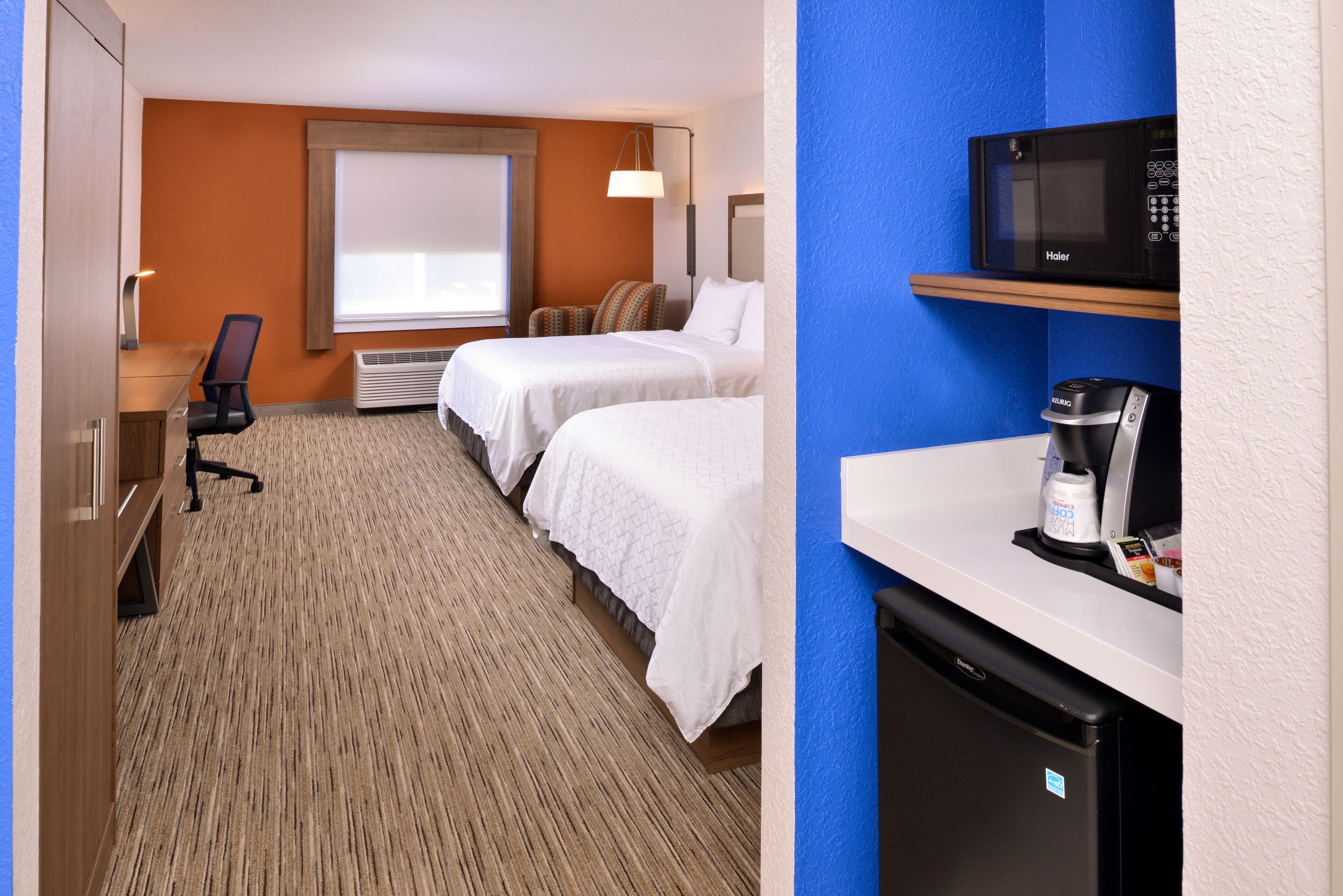 Une chambre d’hôtel avec deux lits, un bureau, une chaise, un four à micro-ondes, une machine à café et un réfrigérateur.