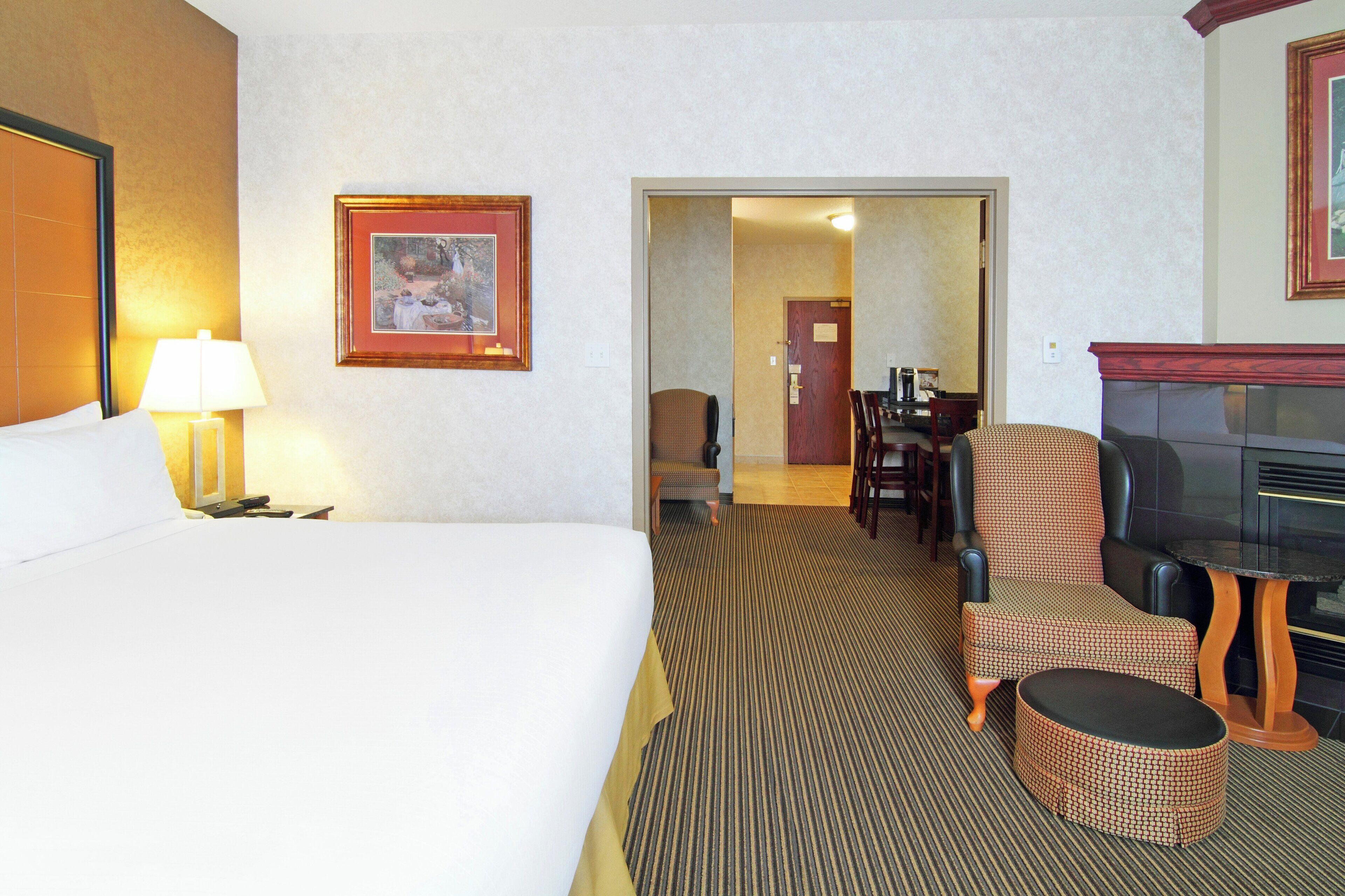 Una camera d'albergo con un letto, una televisione, un'area pranzo e un corridoio che porta a un'altra stanza.