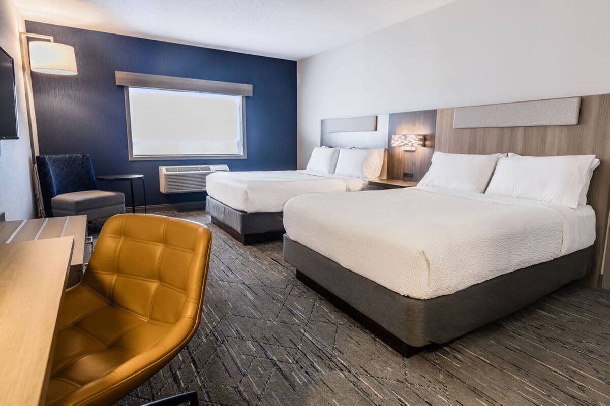 A hotel room with two beds, a desk, a chair, and a large window.