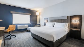 A modern hotel room with a large bed, a desk, a chair, and a window.