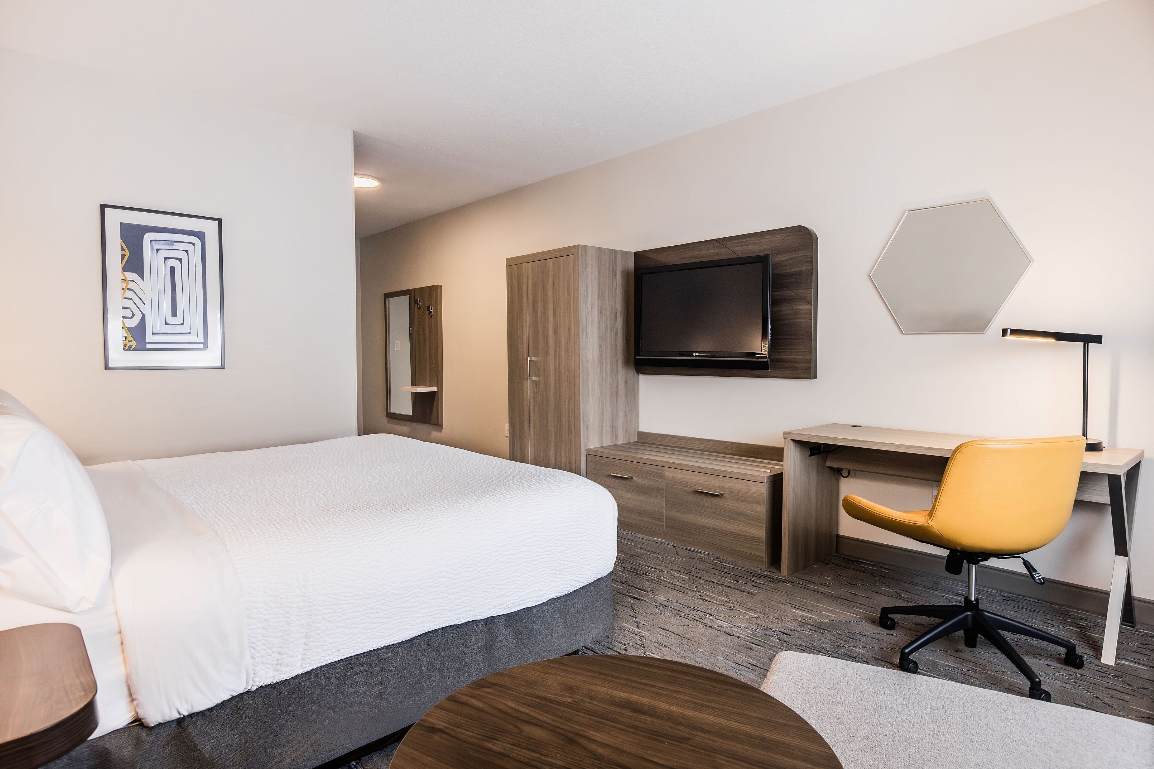 Una habitación de hotel moderna con una cama grande, un escritorio con una silla, un televisor de pantalla plana y un espejo amplio.