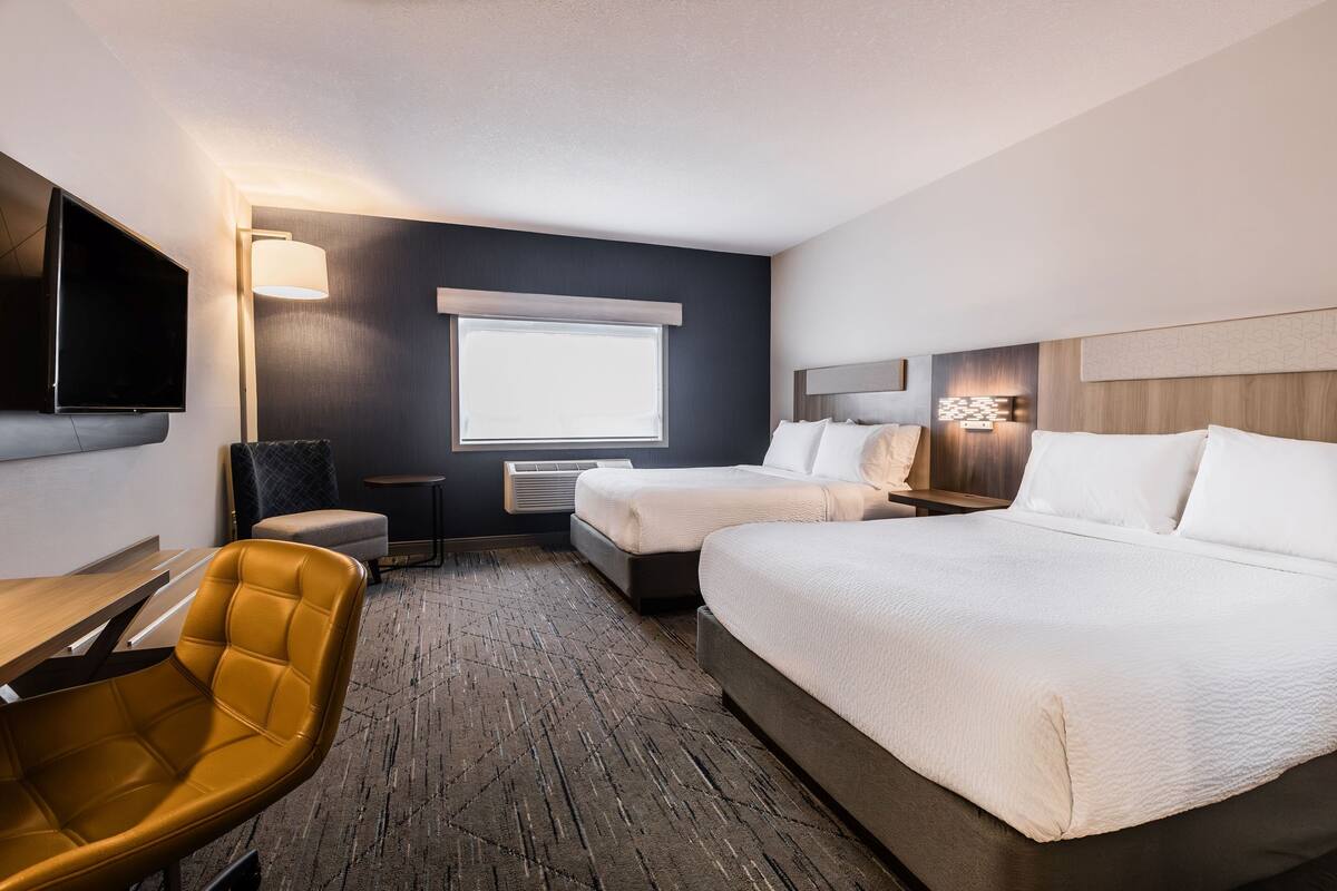 A hotel room with two beds, a desk, a chair, a TV, and a window with blinds.
