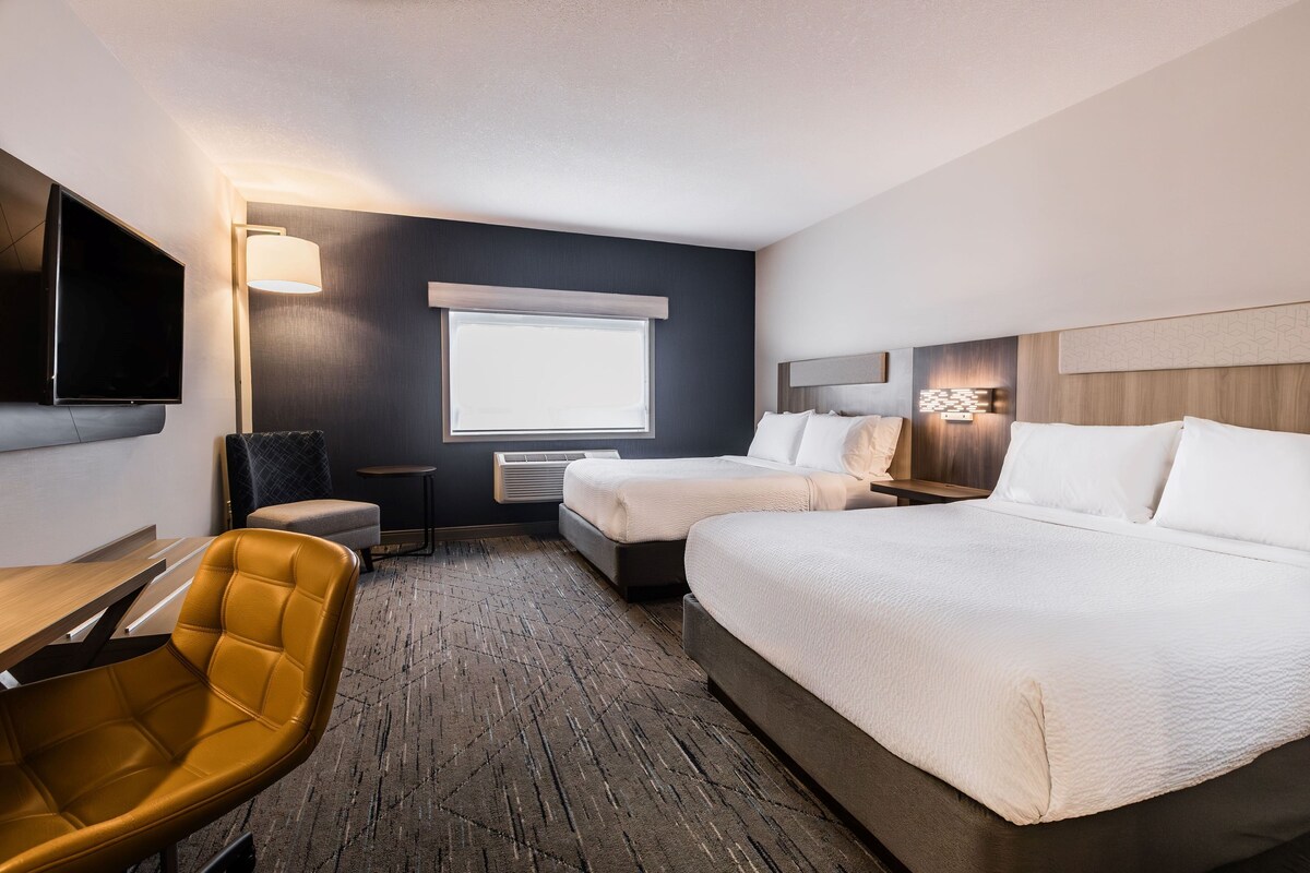 Een hotelkamer met twee bedden, een bureau, een stoel, een televisie en een raam met jaloezieën.