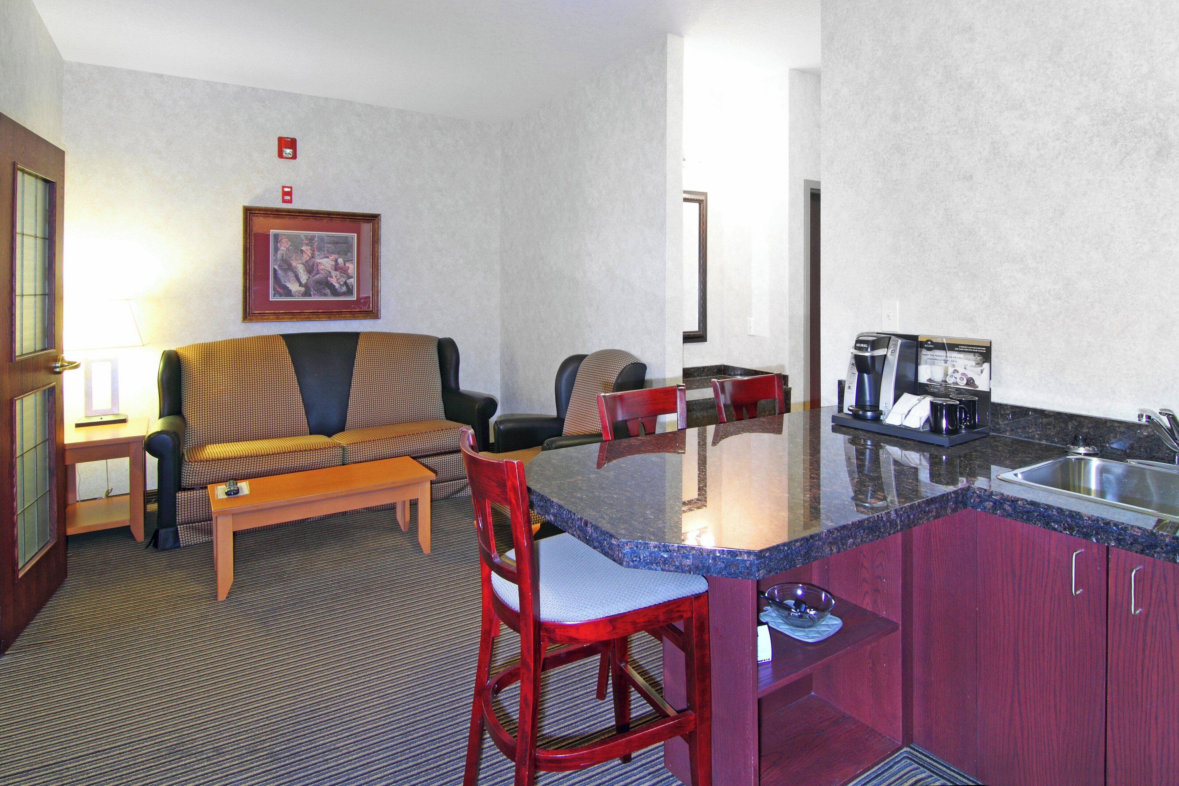 A compact hotel room with a kitchenette, a sofa, a dining table, and a single chair.