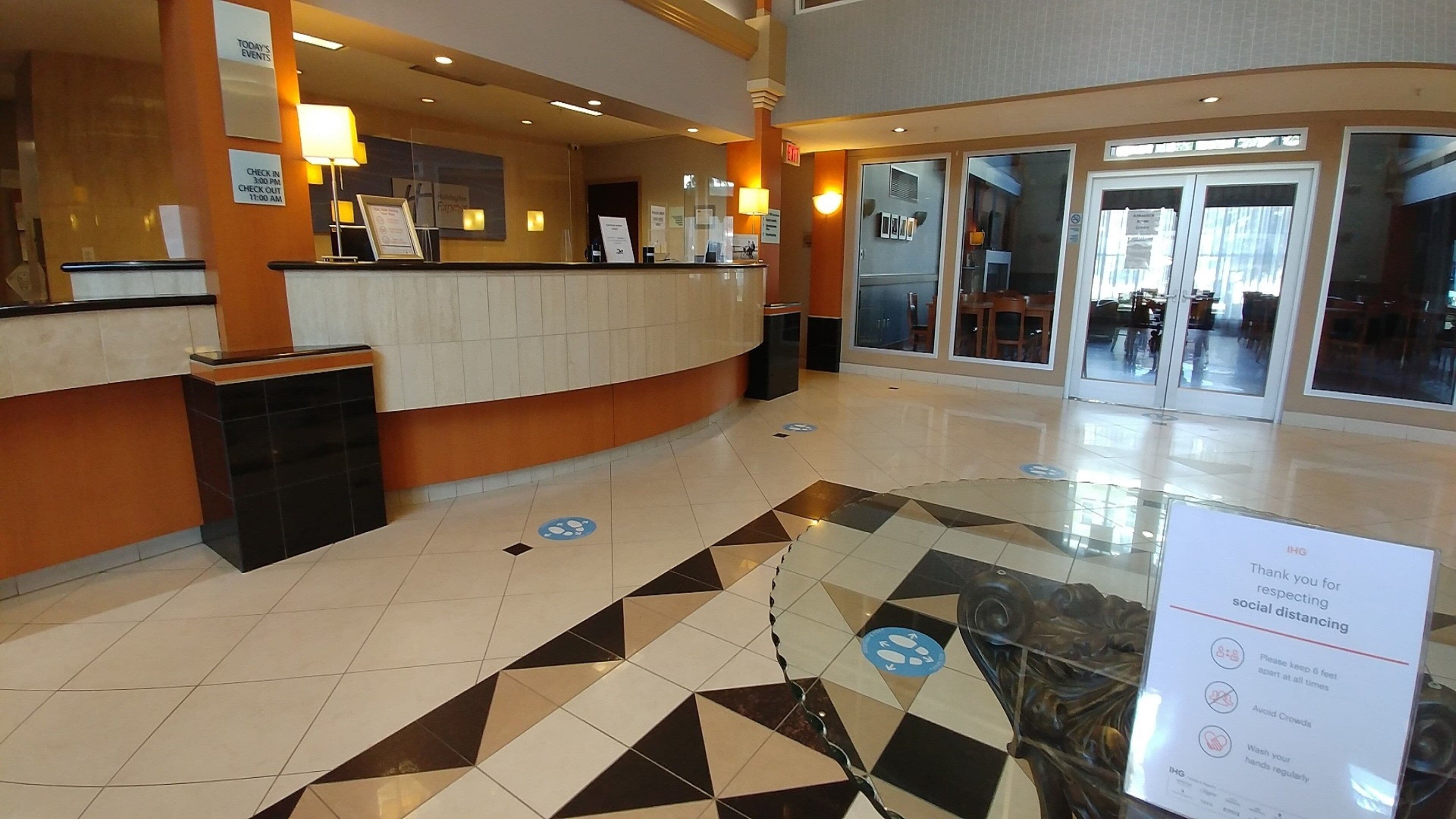 A hotel reception area with a check-in counter, a trash bin, and a sign indicating social distancing guidelines.