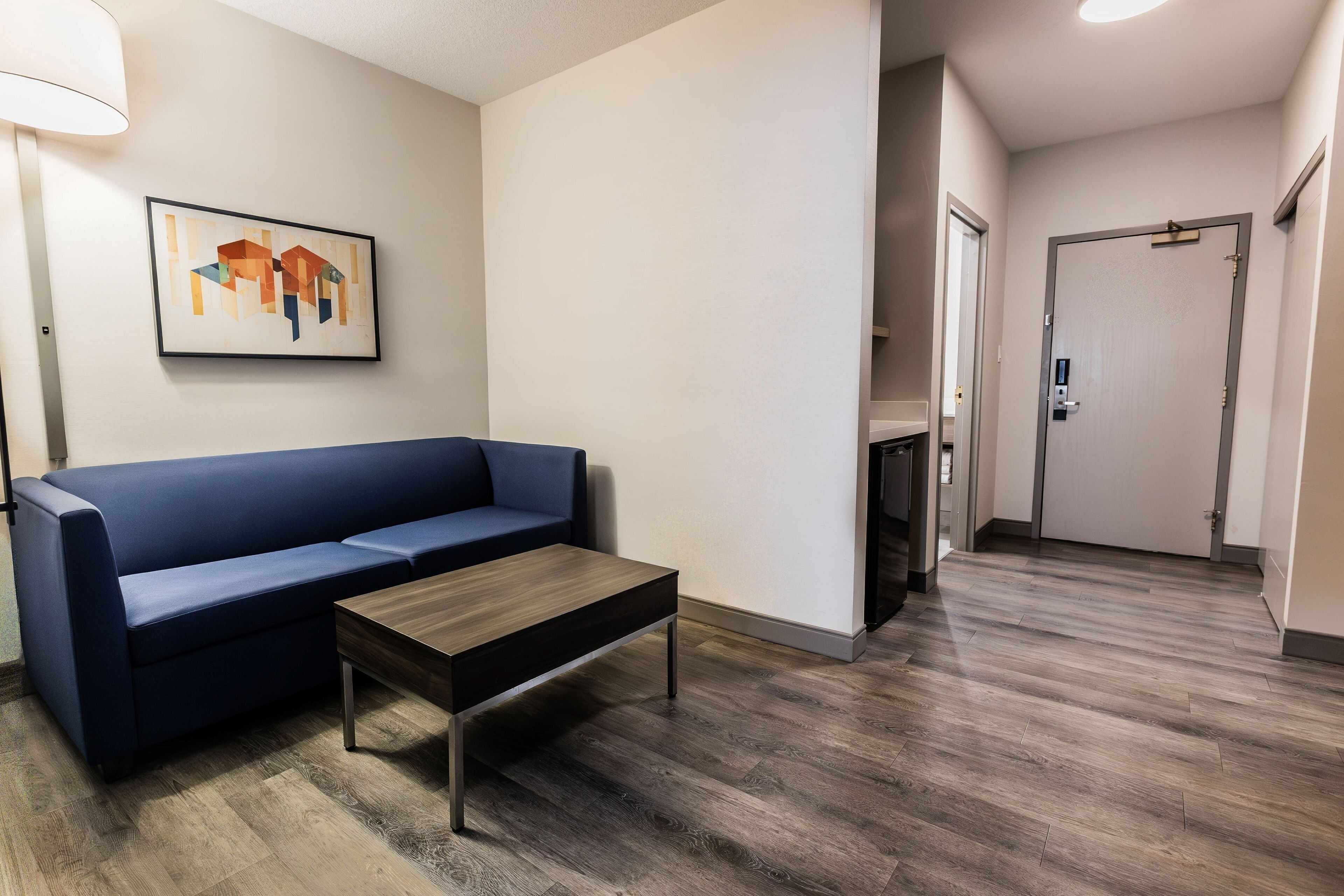A modern hotel lobby with a blue sofa, a wooden coffee table, and a framed abstract painting on the wall.