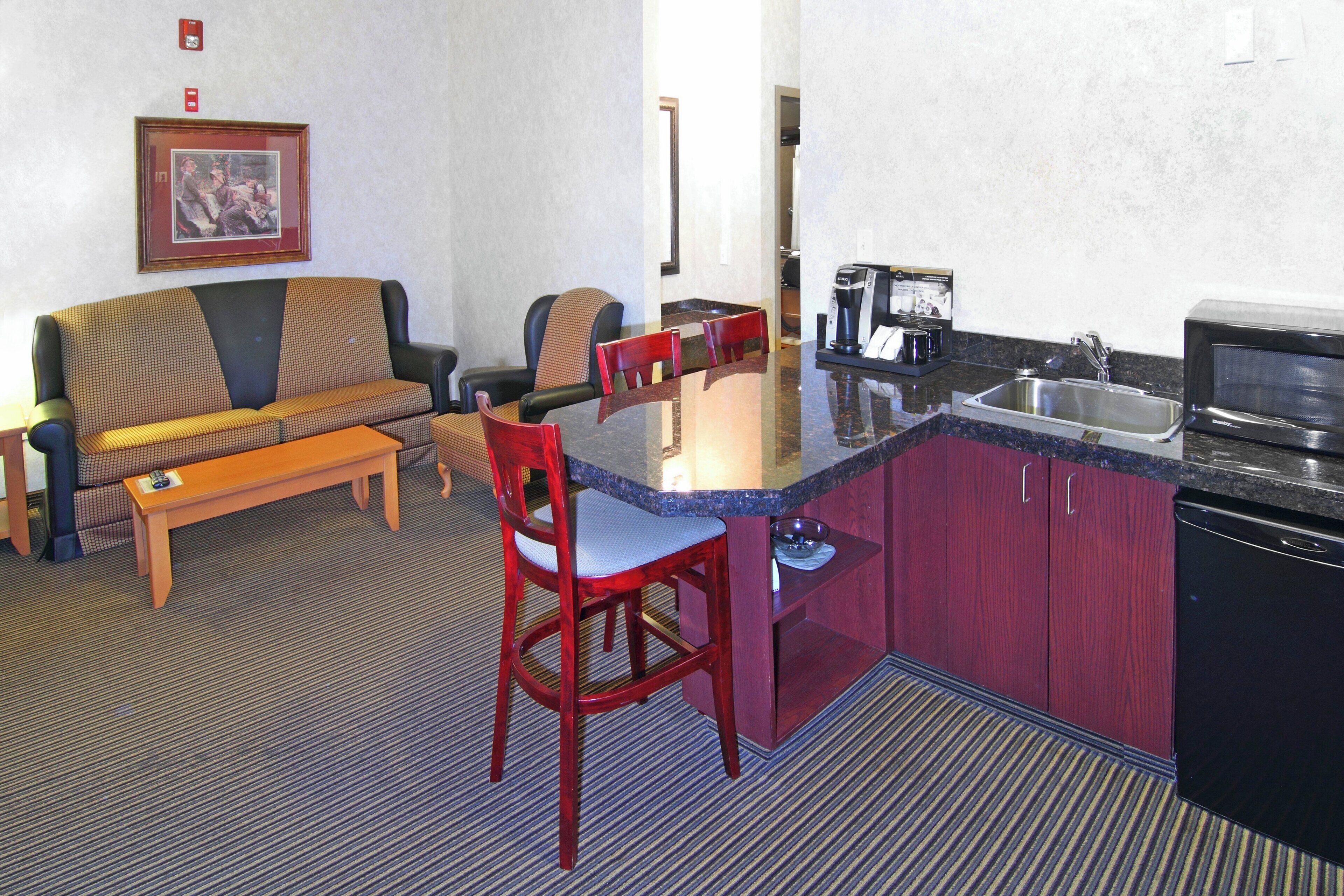 A compact hotel room with a kitchenette, a sofa, a dining table, and a single chair.