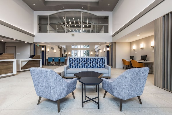 A spacious lobby with a high ceiling, a central seating area with a patterned sofa, and a reception desk.