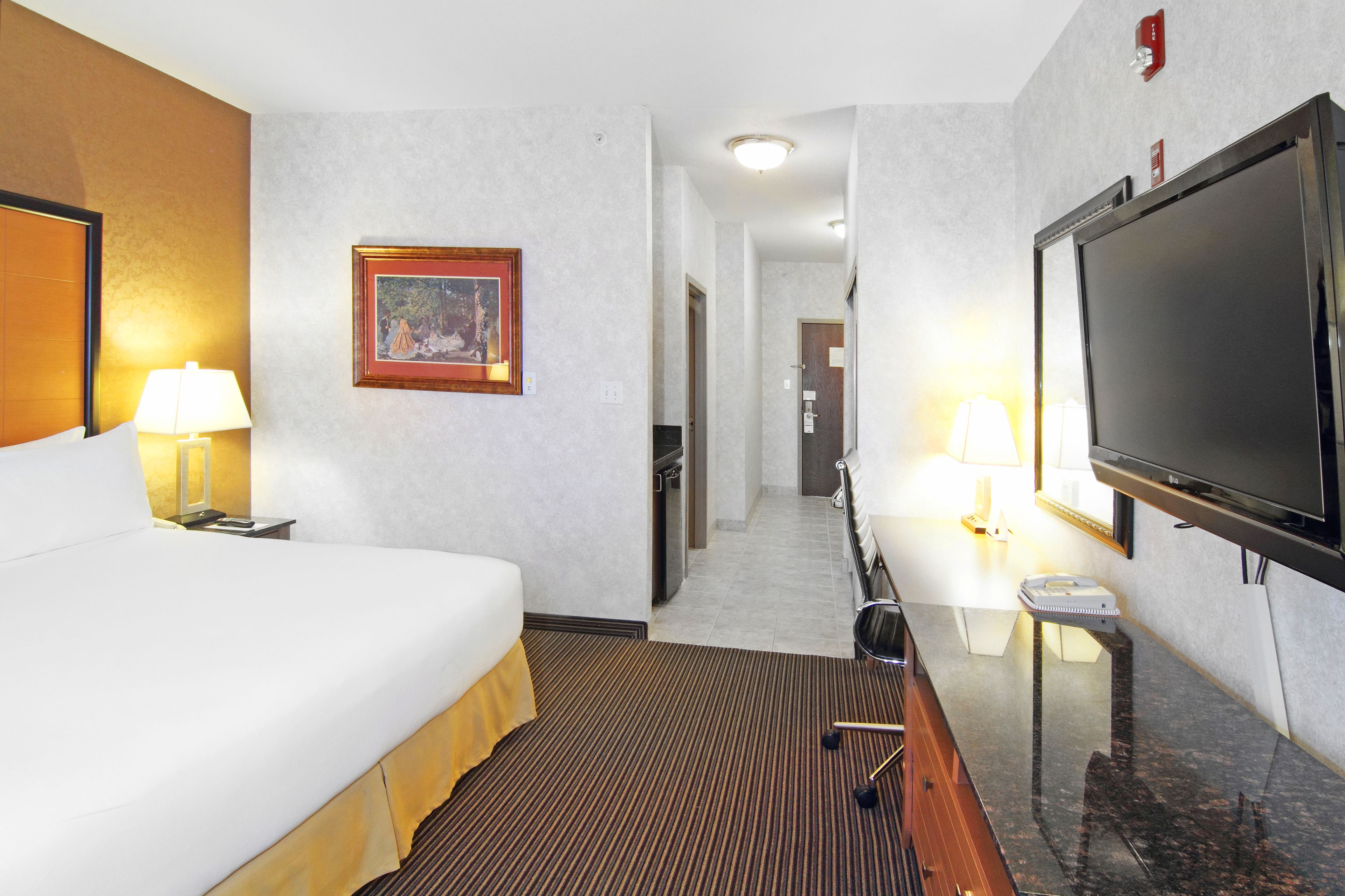 A hotel room with a large bed, a flat-screen TV, a desk with a lamp, and a framed picture on the wall.