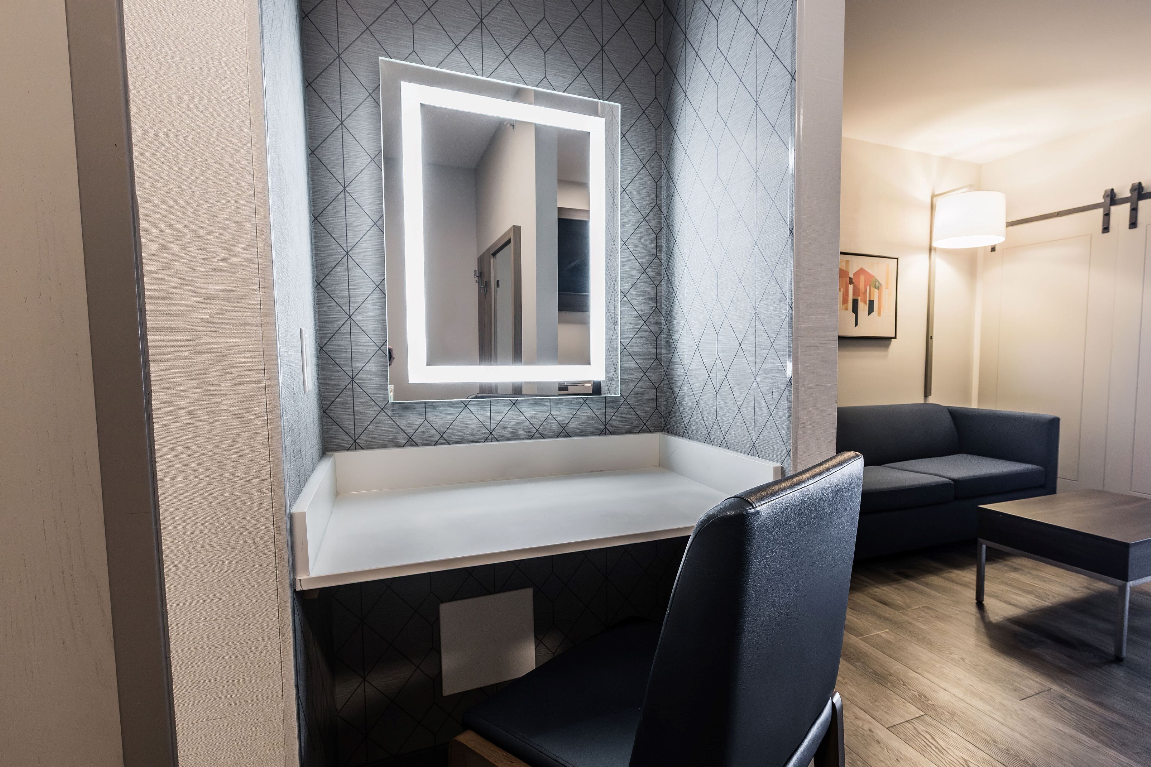 Un baño moderno con tocador, espejo y un sofá en el área de estar contigua.