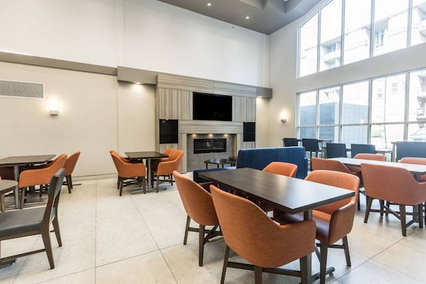 A modern dining area with tables and chairs, a fireplace, and large windows.