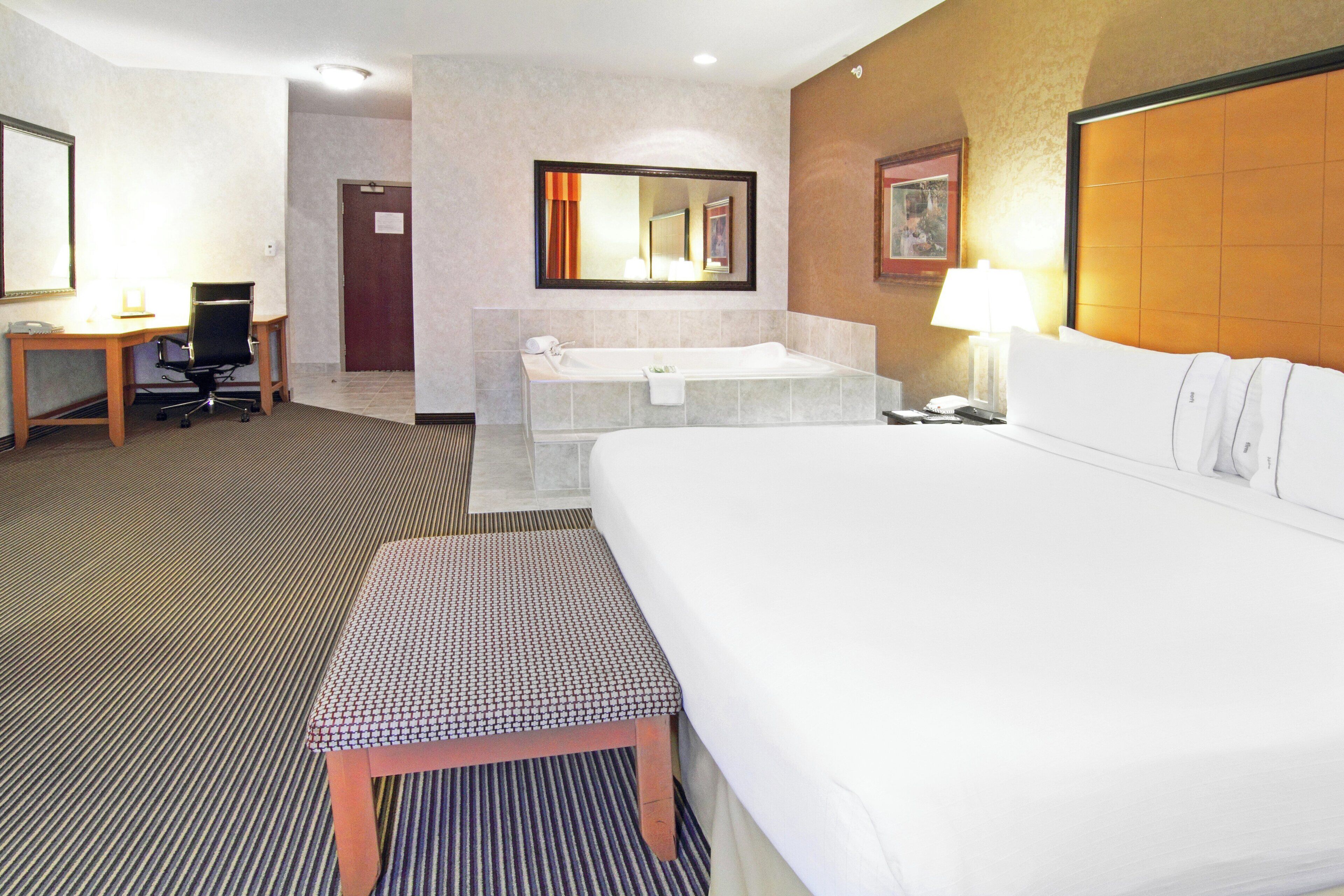A hotel room with a large bed, a desk, a chair, a bathroom with a bathtub, and a mirror.
