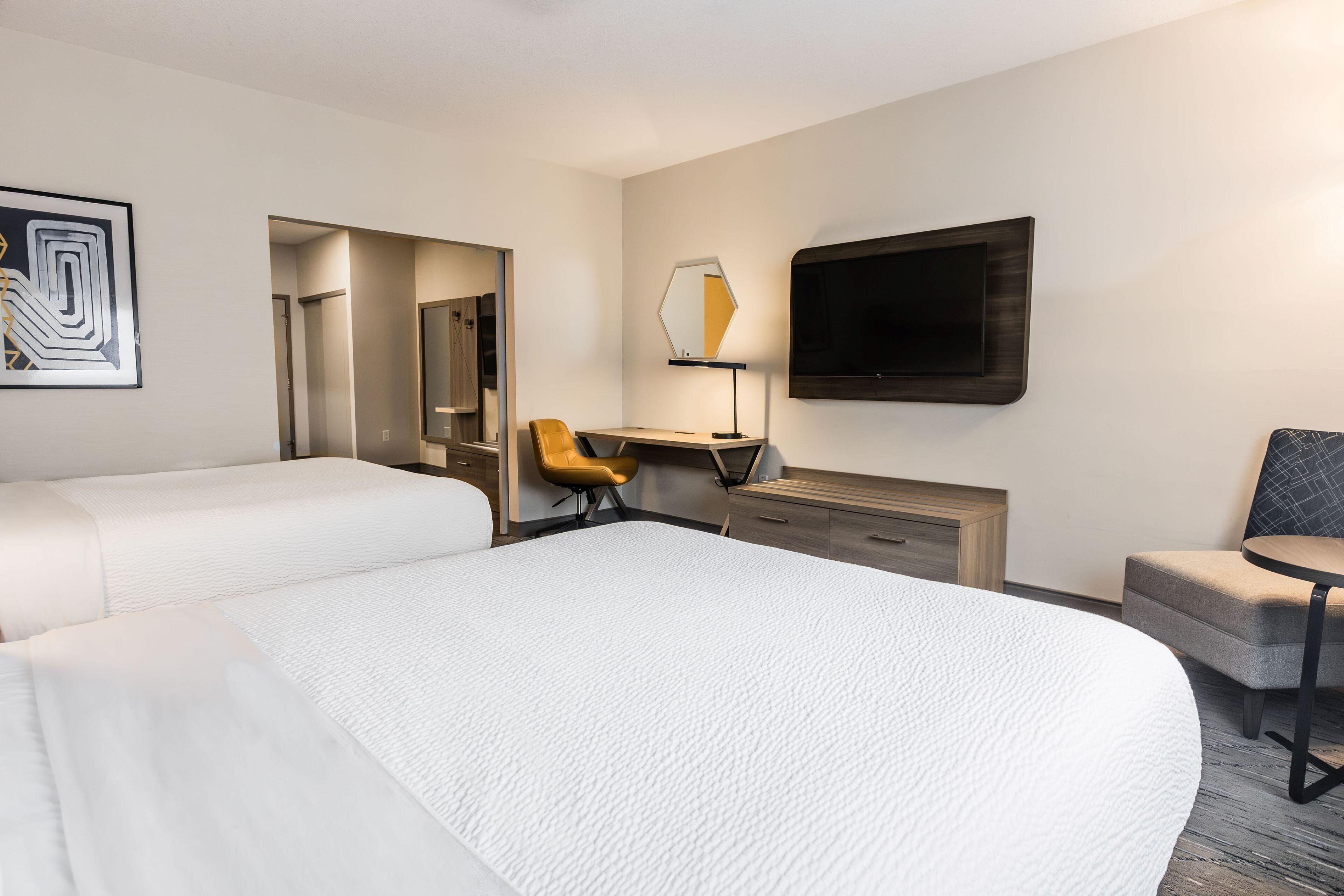 Habitación de hotel con dos camas, un escritorio, una silla, un televisor y un espejo.