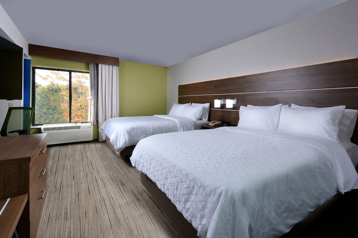 A hotel room with two beds, a desk, and a large window with a view of trees.