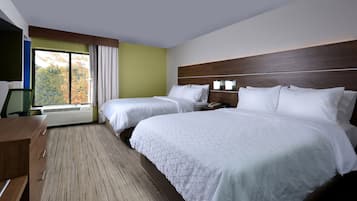 A hotel room with two beds, a desk, and a large window with a view of trees.
