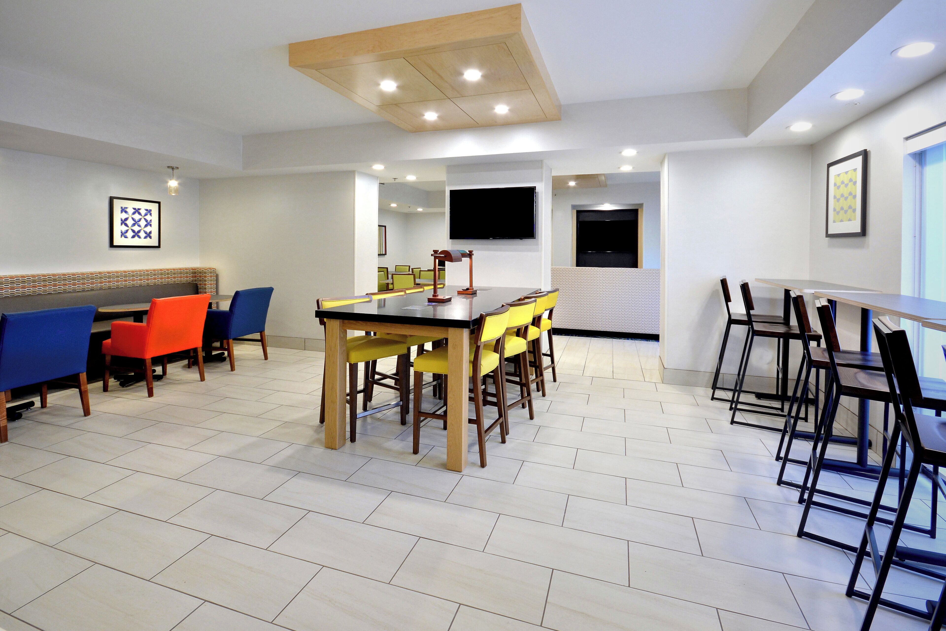 A modern conference room with a large table, chairs, a television, and a patterned wall.