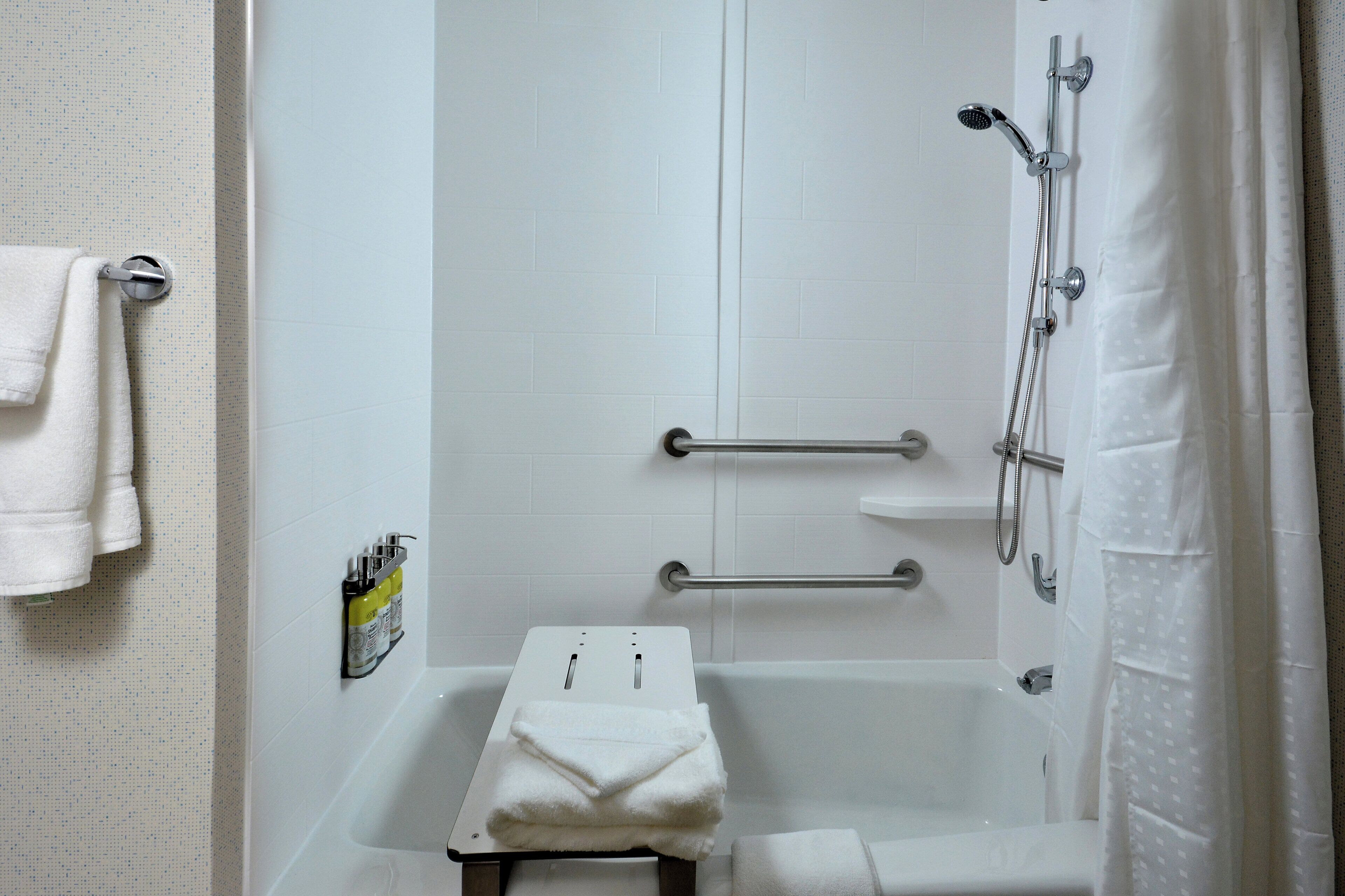A bathroom with a bathtub, a shower, a towel rack, and a soap dispenser.