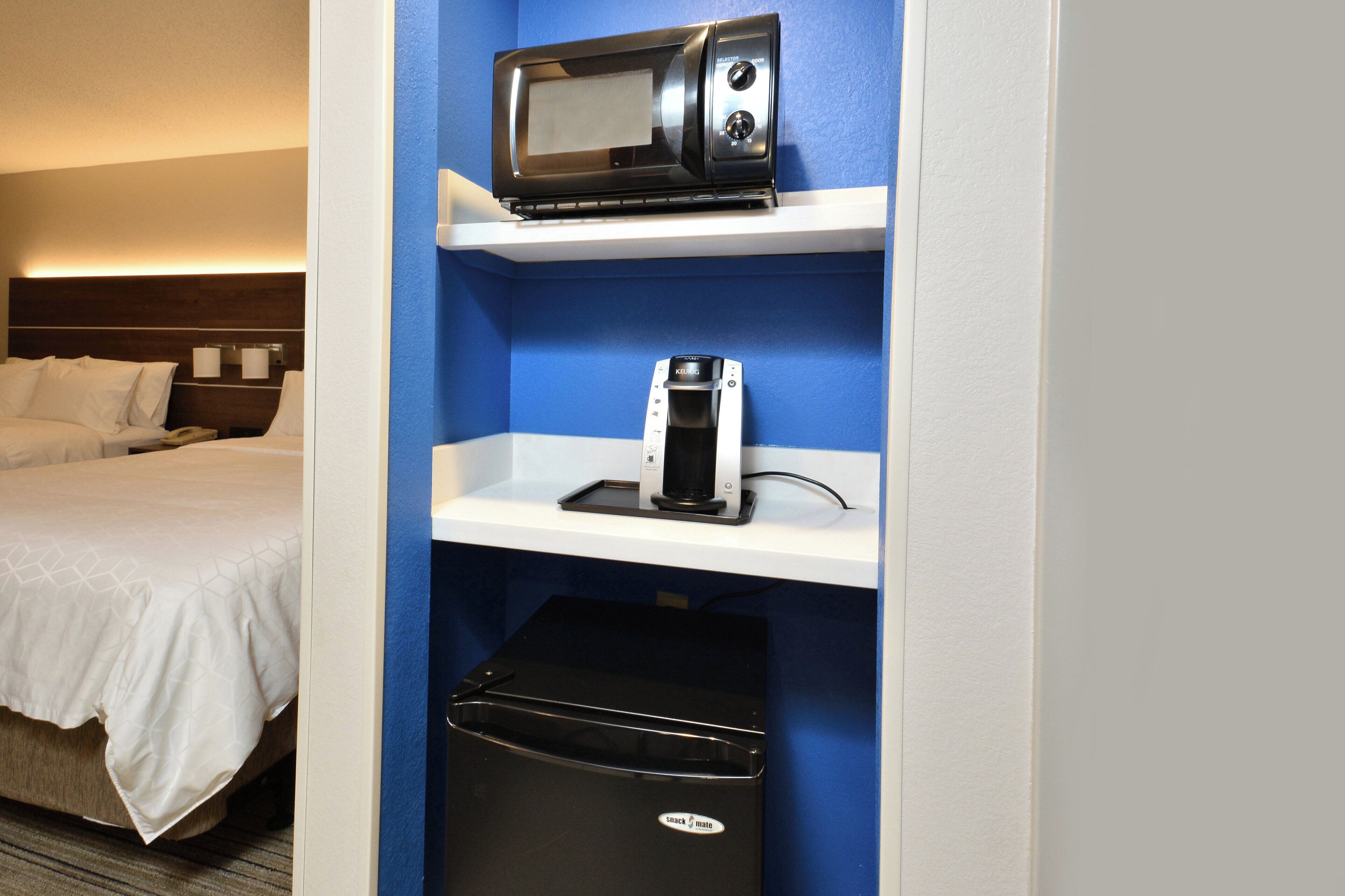 Habitación de hotel con cama, microondas, cafetera y basurero.