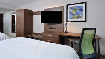 A hotel room with a bed, a desk with a flat-screen TV, a chair, and a framed picture on the wall.
