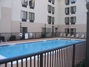 A swimming pool with a metal railing, surrounded by a building with multiple windows and a sign indicating no lifeguard on duty.