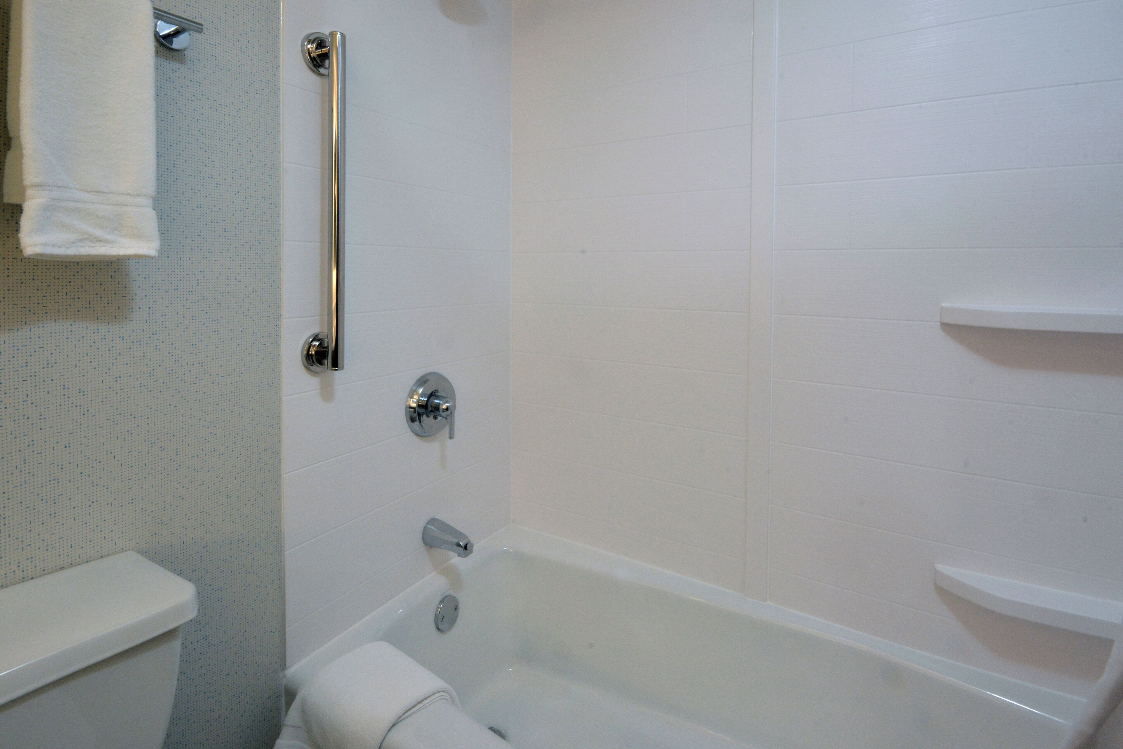 A bathroom with a white bathtub, a toilet, and a shower area with a grab bar.