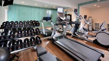 A gym with treadmills, elliptical machines, and a rack of dumbbells.