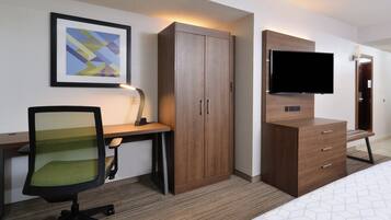A hotel room with a bed, a desk with a chair, a wardrobe, a television, and a framed picture on the wall.