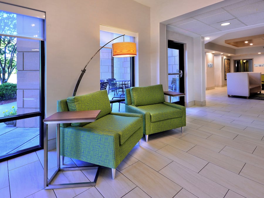 A hotel lobby with green upholstered chairs, a floor lamp, and a television screen.