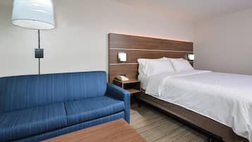 Una habitación de hotel con una cama, un sofá azul, una mesa de madera y una mesita de noche con una lámpara.