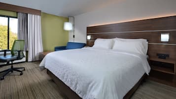 Habitación de hotel con una cama grande, un escritorio con silla, una mesita de noche y una ventana con cortinas.