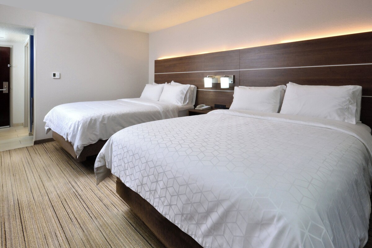 A hotel room with two beds, a wooden headboard, a nightstand with a phone, and a carpeted floor.