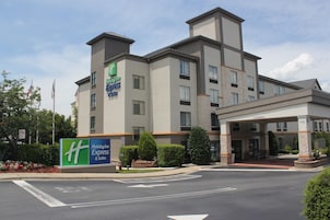 A Holiday Inn Express & Suites hotel with a modern design, featuring a large sign, a covered entrance, and landscaped surroundings.