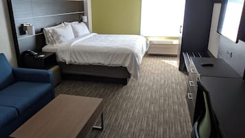 A hotel room with a bed, a desk, a chair, a sofa, and a television.