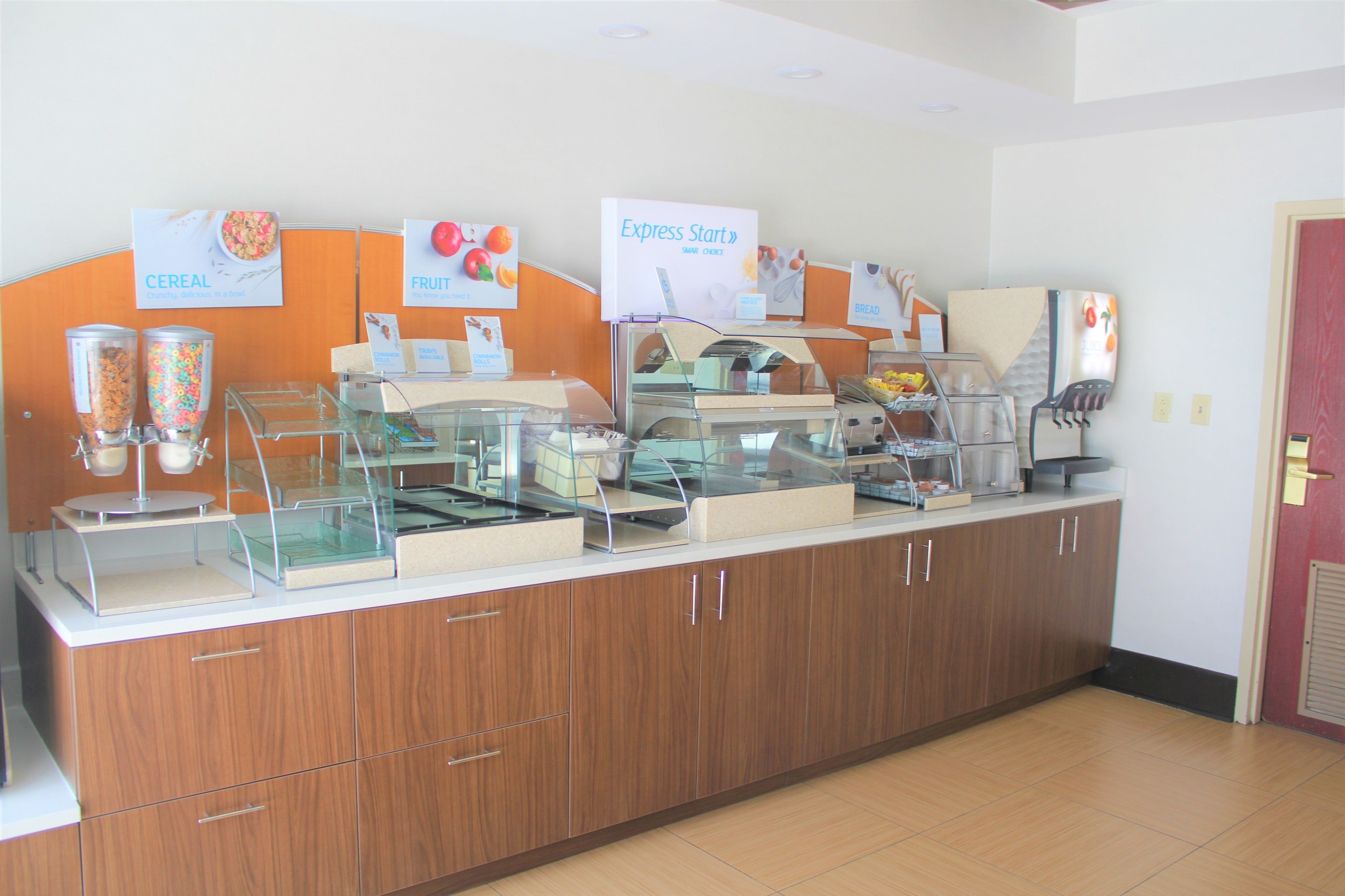 Buffet de café da manhã com seções identificadas para cereais, frutas e pão.