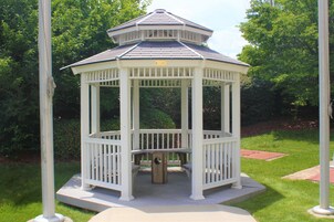 A white gazebo with a hexagonal roof, surrounded by grass and trees.