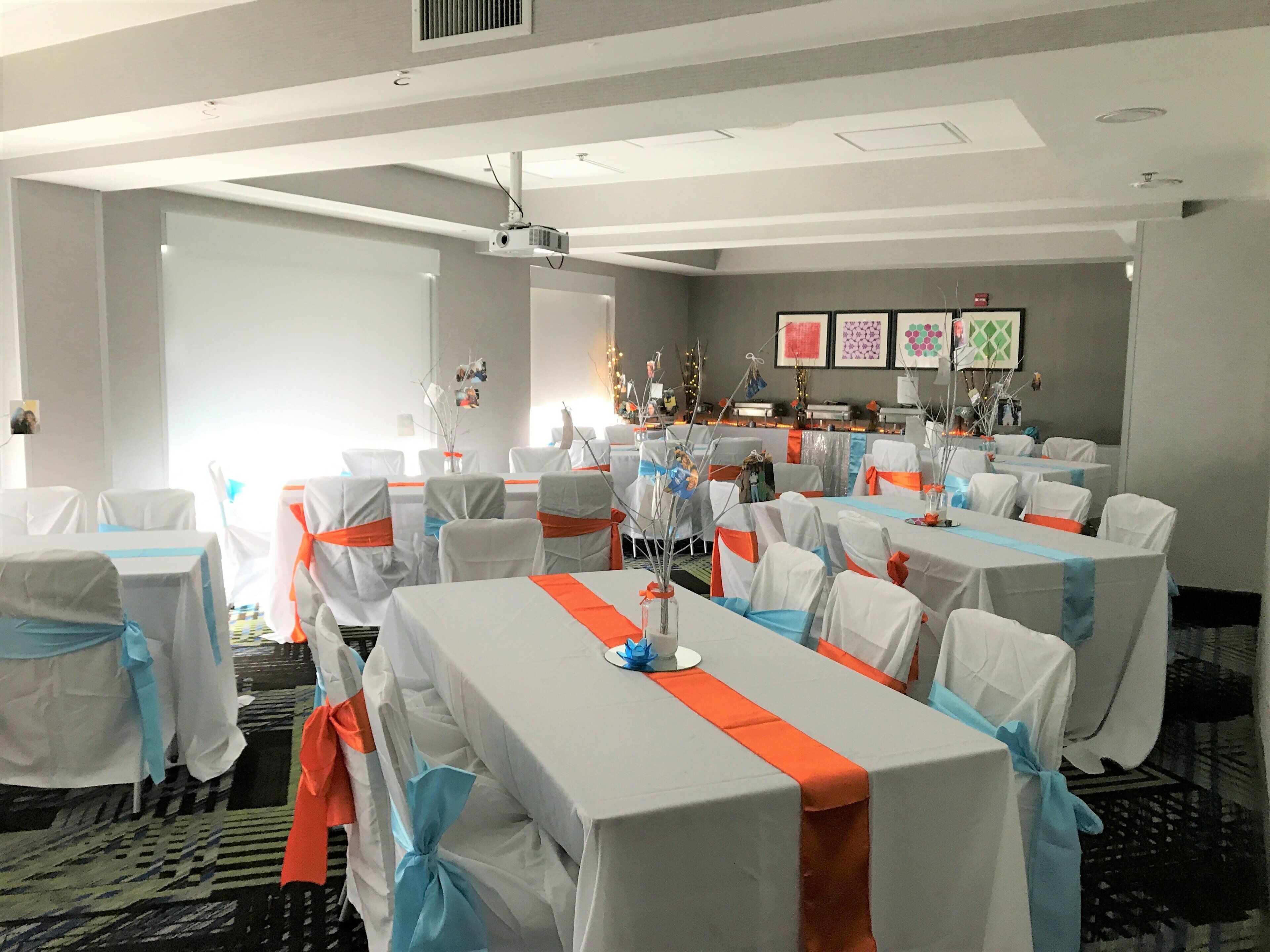 A conference room with tables covered in white tablecloths and orange sashes, arranged in rows.