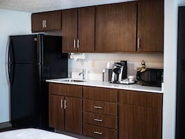 A modern kitchen with dark wooden cabinets, a black refrigerator, a coffee maker, and a microwave.