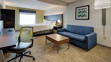 Quarto de hotel com uma cama, uma escrivaninha, uma cadeira, um sofá e um abajur.