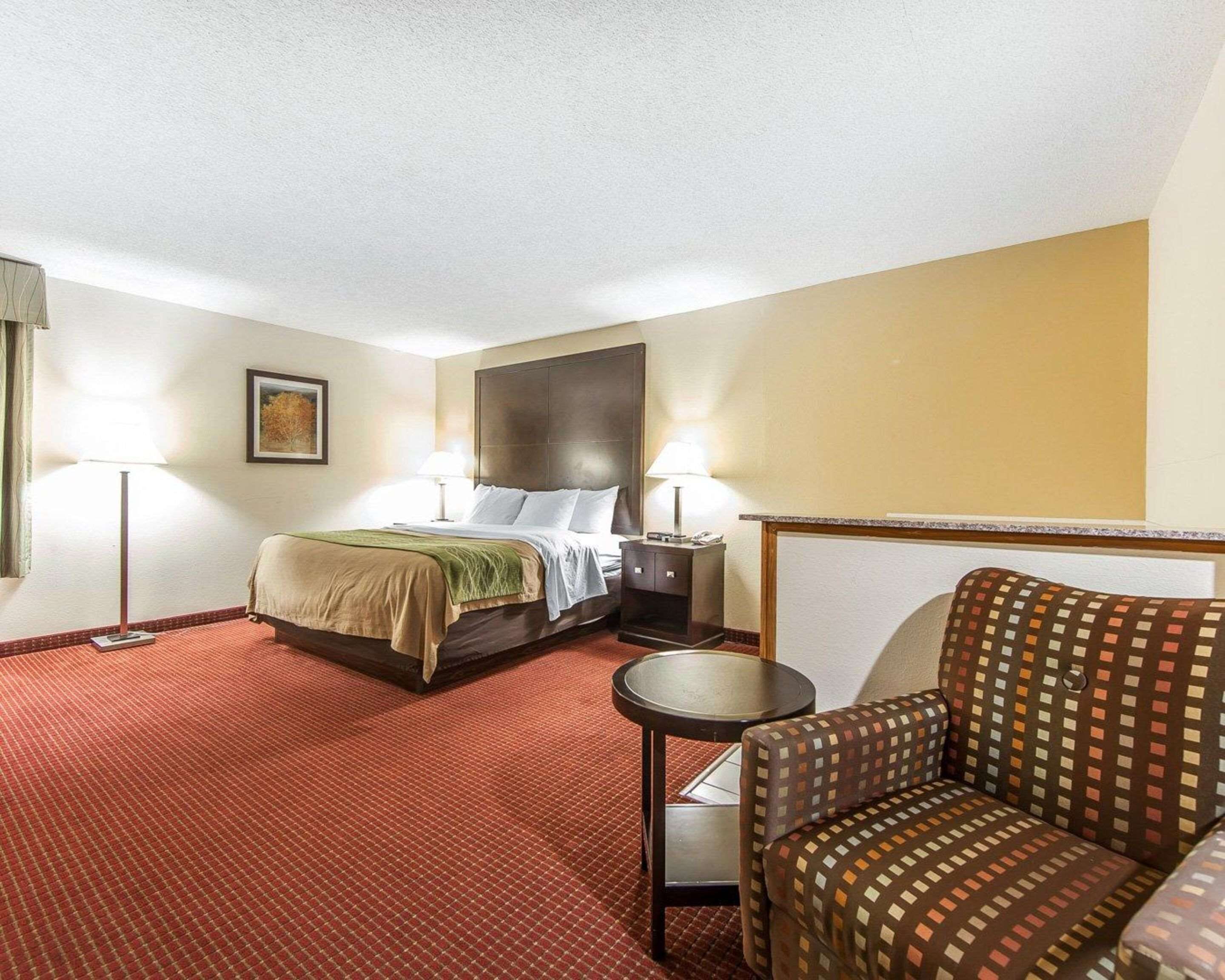 Una habitación de hotel con una cama, dos mesitas de noche, una silla y una pequeña mesa.